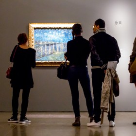 People looking at a painting, and listening to audio guides, in an exhibition