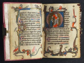 an image of a medieval book showing gothic text will illustrations in red, gold and blue on the edges of the page and text