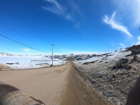 a landscape photo of a road in Kinngait, Nunavut featuring a bright blue sky and the unpaved road coming from the lower left corner towards the centre horizon