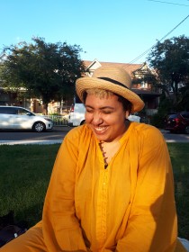 Photograph of a smiling woman wearing a beige sun har and orange clothes