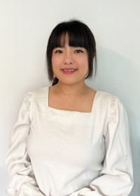 Headshot of an east asian woman with black bangs and straight hair, wearing a white blouse and smiling