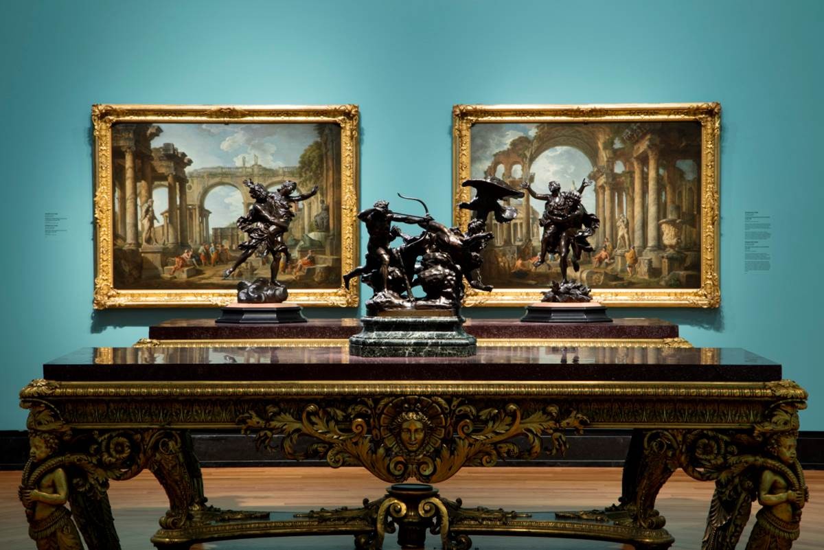 Ornate table with statues on top and paintings hanging behind
