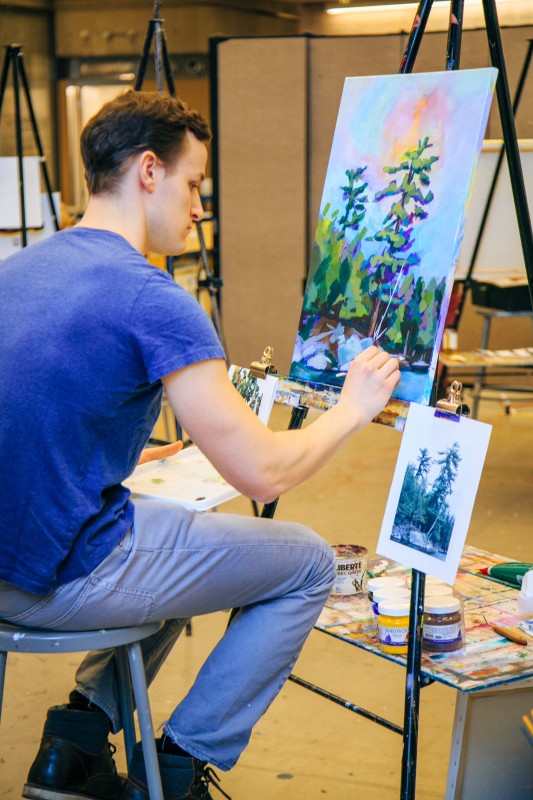 man sitting painting at easel