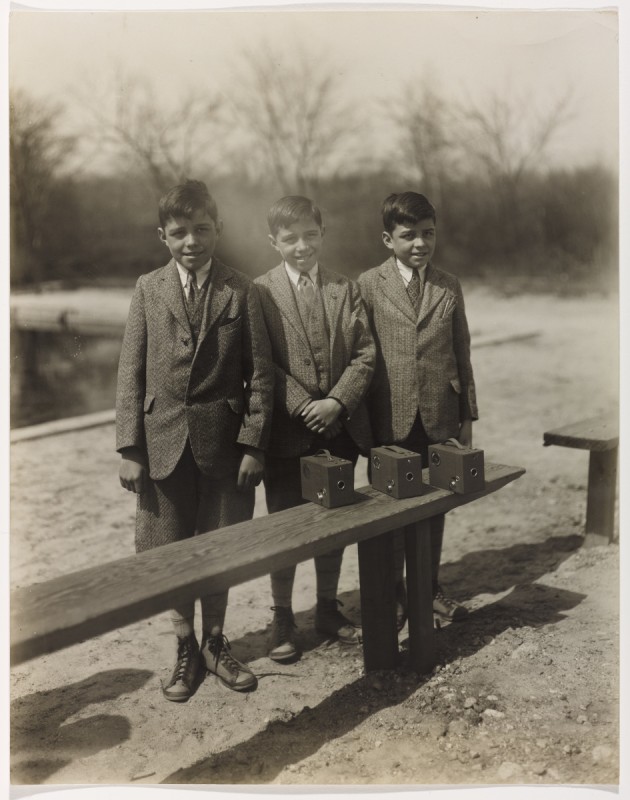black and white photo of triplets dressed in suits standing behind a bench outdoors