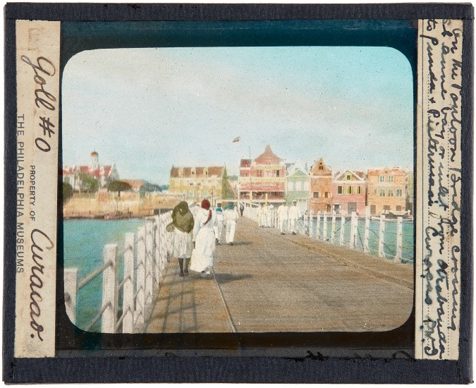 On The Pontoon Bridge Crossing St. Anne Bay or Inlet from Otrobanda to Punda and Pietermaii, Curaçao, around 1910. Lantern slide: hand-painted gelatin silver on glass.