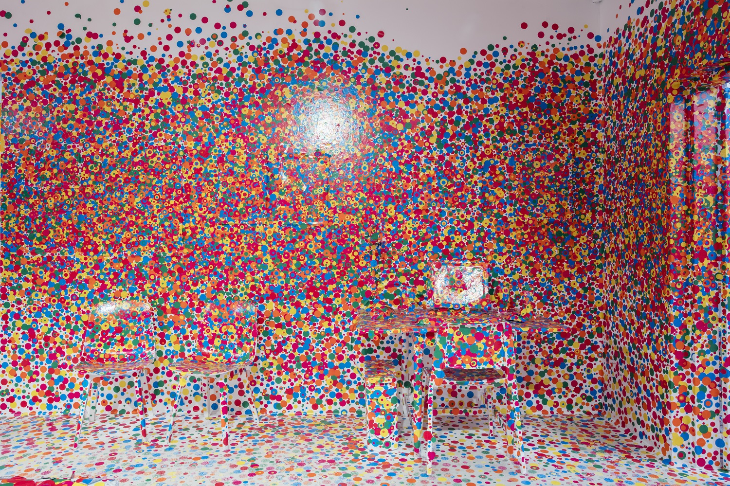 A computer desk and chairs covered in bright polka dots as part of Yayoi Kusama's The Obliteration Room.