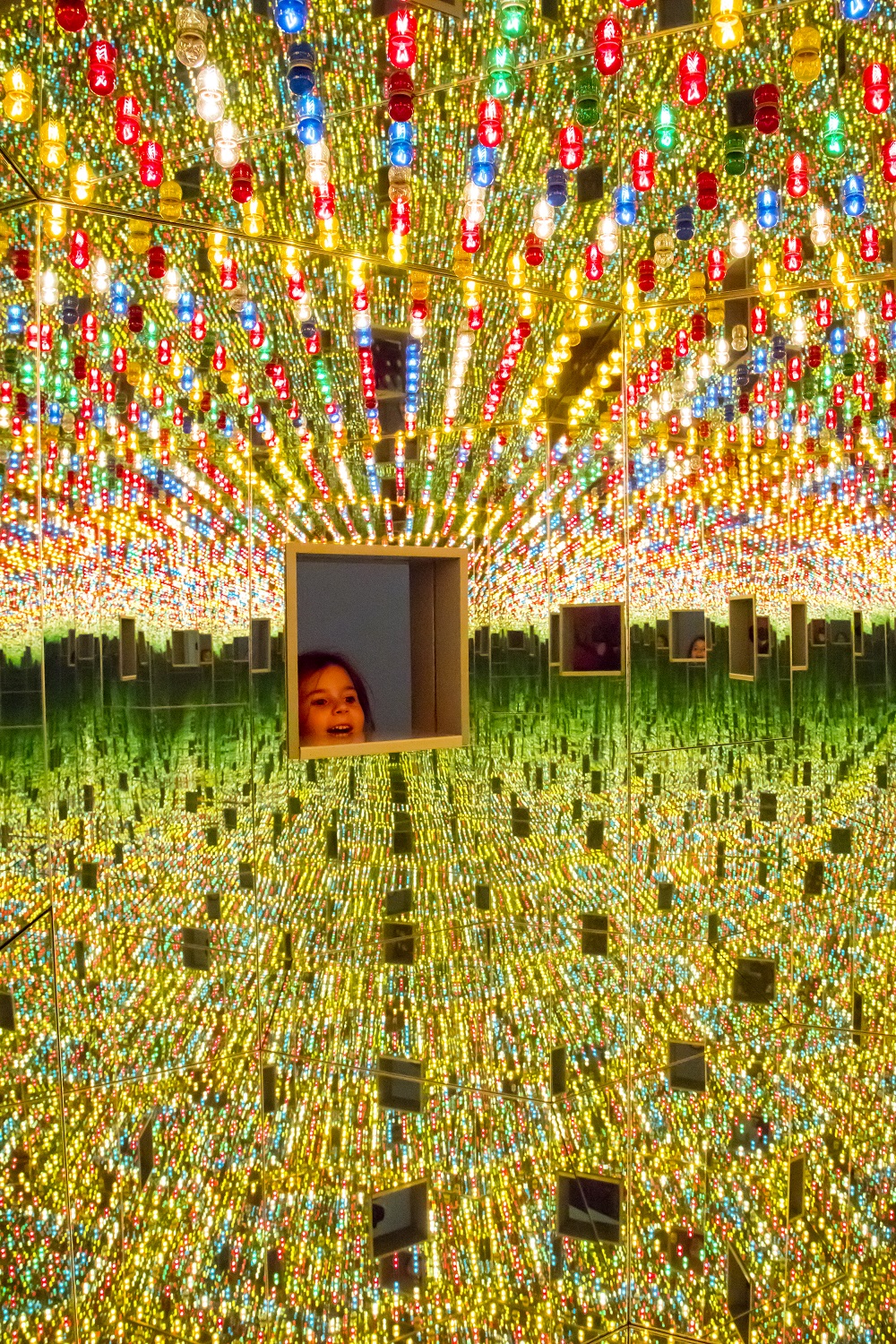 A small child's face peers through one of the peep holes in Yayoi Kusama's Infinity Mirror Room "Love Forever."