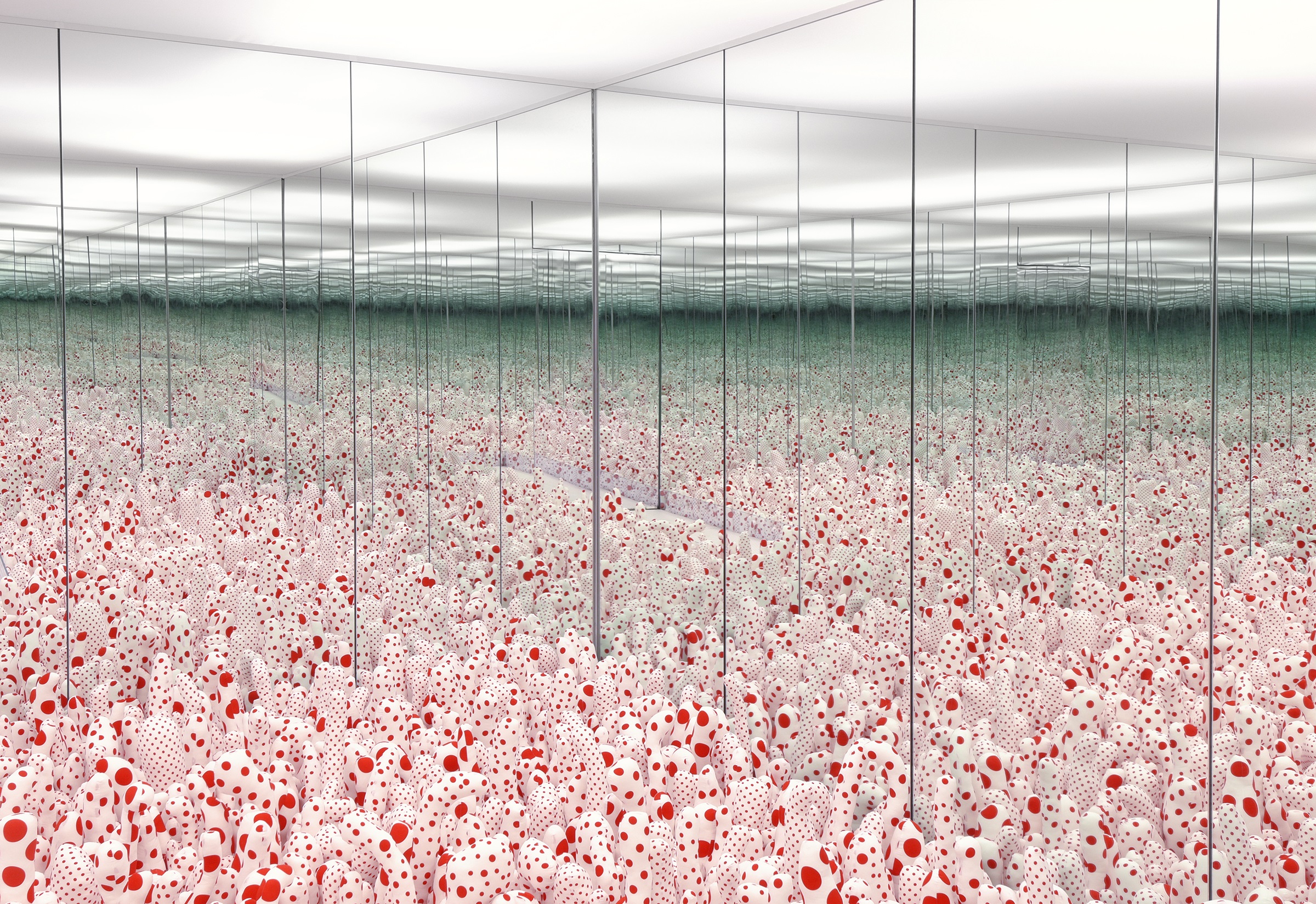 Inside one of Yayoi Kusama's Infinity Mirror Rooms, with mirror walls that reflect a floor of soft white and red polka-dotted sculptures on and on.