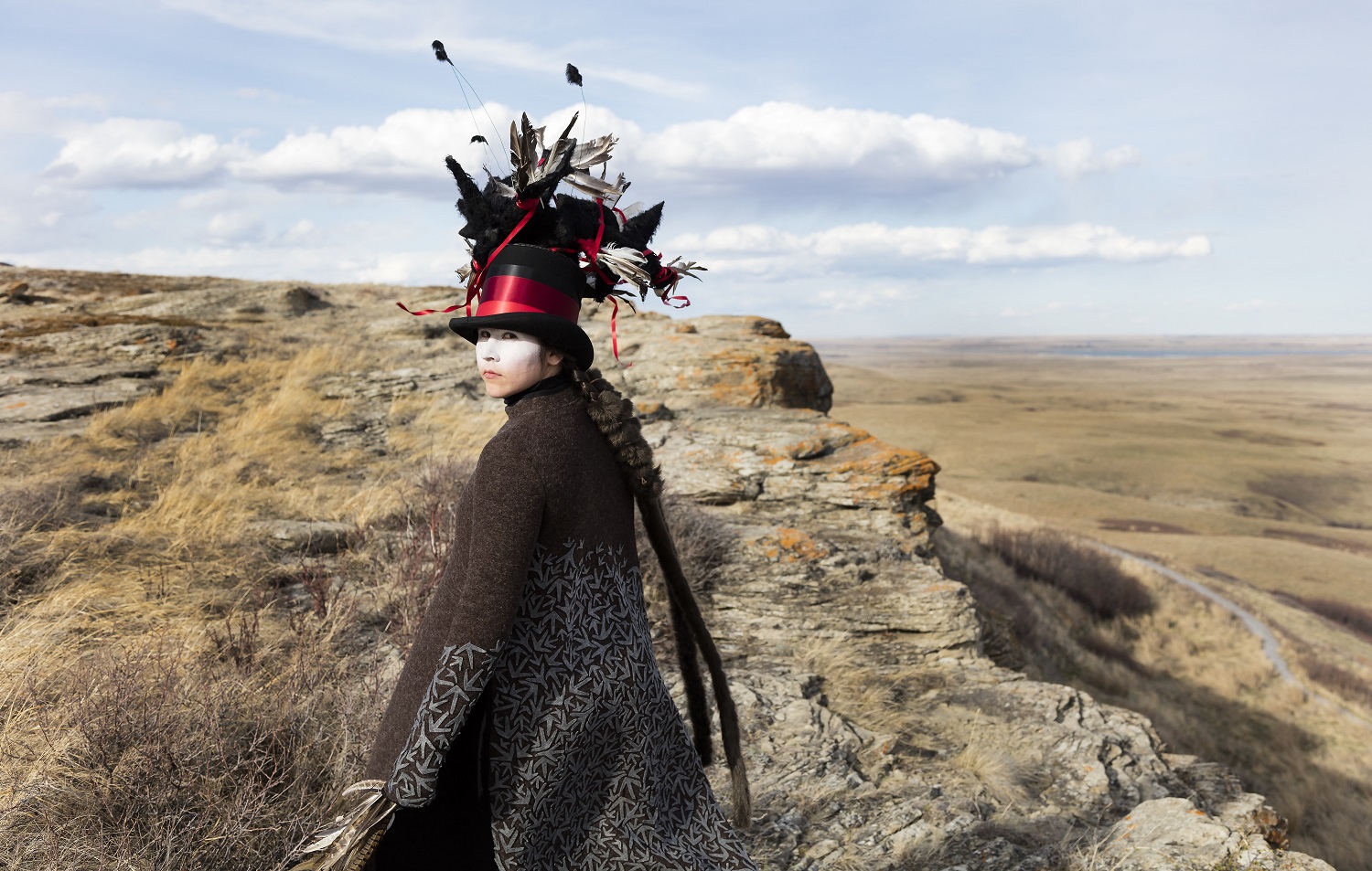 a photo of a woman with facepaint and a large hat standing by a cliff