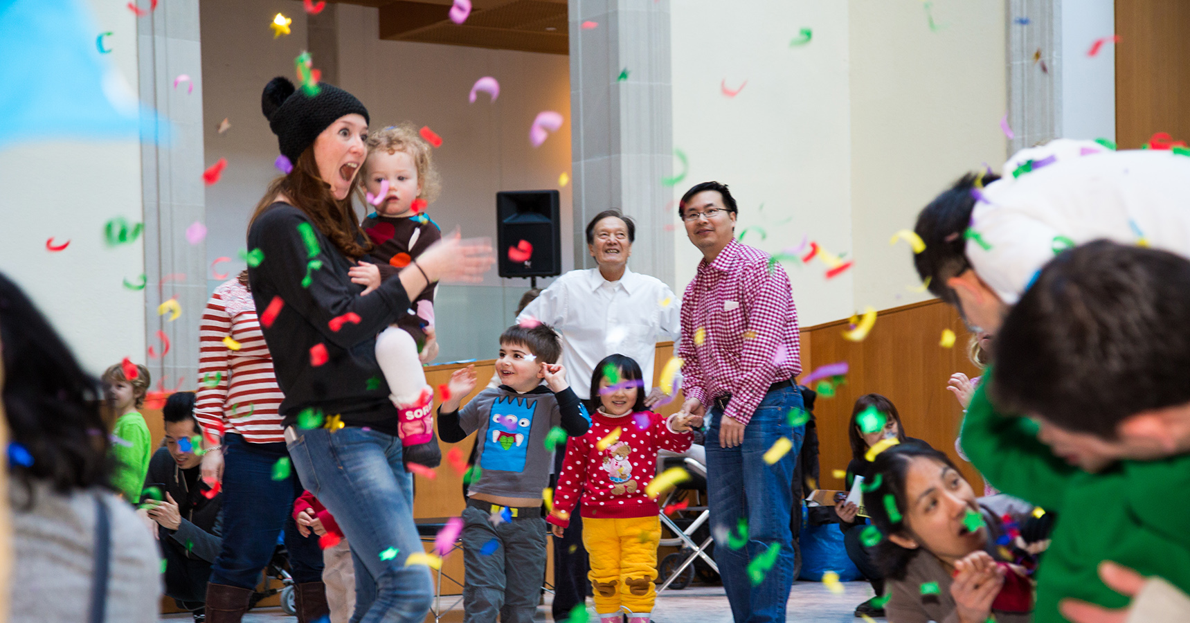 A group of adults and children play in a room full of falling confetti