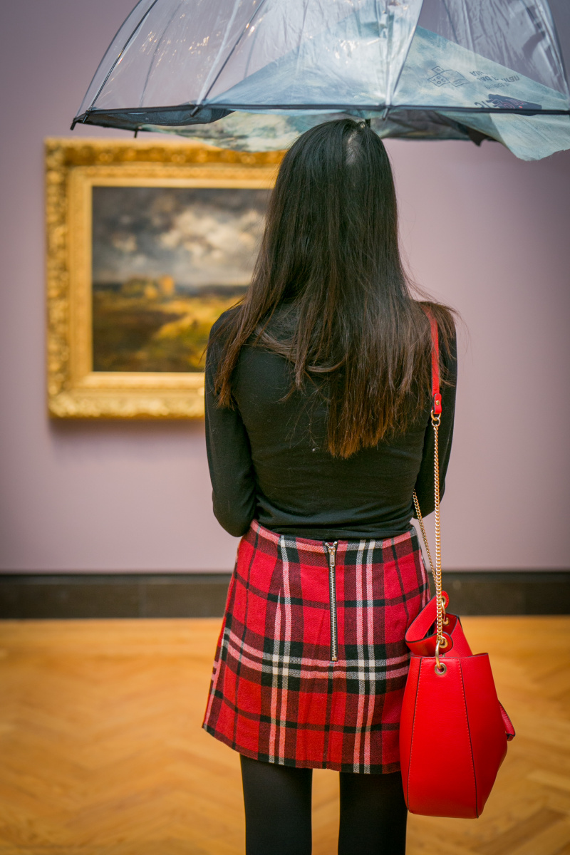 Woman looks at a painting holding an umbrella.