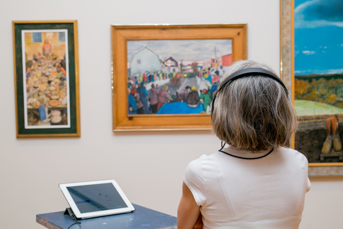 A woman looks at a painting with headphones on.