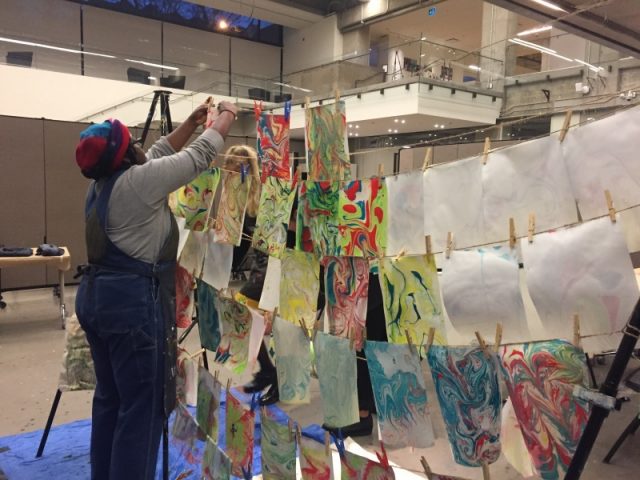 A women hanging up painted paper on a line