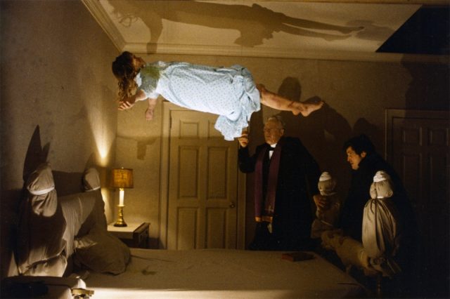 I girl levitating above a bed, with two priests at the bed post