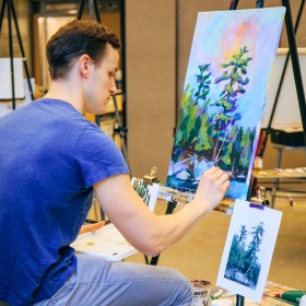 man sitting painting at easel