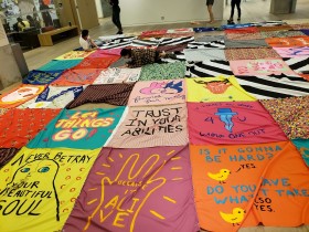 hand painted messages on brightly coloured fabrics and then stitched together to create a large scale quilt