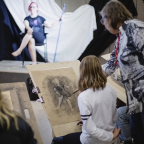 instructor with student in life drawing class, model in background