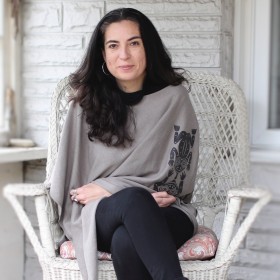 Writer and Journalist Tanya Talaga sitting on a white-painted porch in a white wicker chair