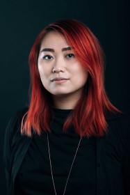 Dark headshot of artist Shellie Zhang in a black top with red hair