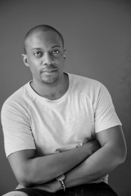 black and white portrait of artist Hank Willis Thomas wearing a white tshirt with arms folded