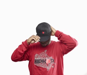 Image of DJ Grumps wearing a black ball cap and red sweater. 