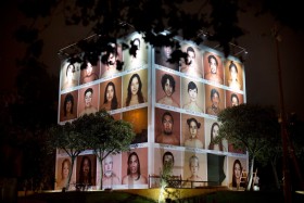 photo of a large cube installation covered in portraits of people with the background matching their skin tone