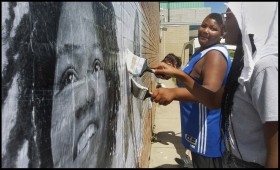 photo of Capturing Belief participants Rah and Dejuan pasting onto a brick wall large black and white portrait of a young Black person smiling