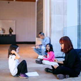 Two adults and two children sitting on the ground with art books