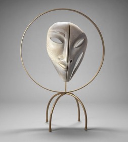 a sculpture of a mask carved in white stone, mounted on a base of four metal legs and encircled by a metal ring
