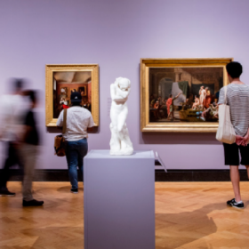 Members walking through the gallery looking at framed art work and a sculpture.  