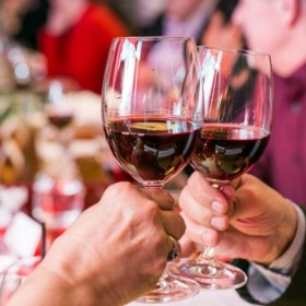 Two glasses of red wine at a dinner event, they are in a cheers gesture where the glasses are meeting. 
