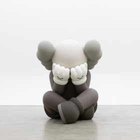 photo of KAWS sculpture Separated, featuring Companion sitting cross legged, hands covering their eyes. Sculpture is bronze and painted in shades of gray
