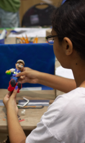 A young girl with glasses works on sculpting a human figure out of different coloured clay