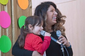 Parent and child both holding microphones smiling with a polkadot curtain behind them.