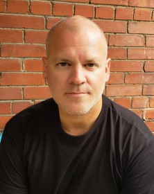 Scott Everingham wearing black crew neck, posing in front of brick wall