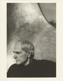 black and white photo pf artist Henry Moore, in profile, in front of his sculpture Two Forms