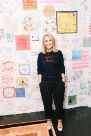 Diana Weymar smiling and standing in front of a wall of quilted squares of various types and patterns