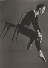 Merce Cunningham, performing, mid jump, with a chair strapped to his back