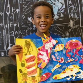 child holding up collage artwork