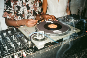 DJ booth with a vinyl record player and mixing board with hands