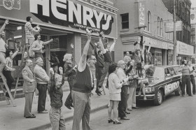 Black and white photograph of a group of people celebrating in 1974 in front of the Henry's location on Church Street in Toronto.