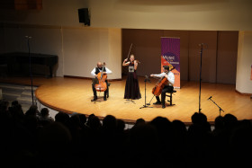 Three musicians on stage, one violinist and two cellists