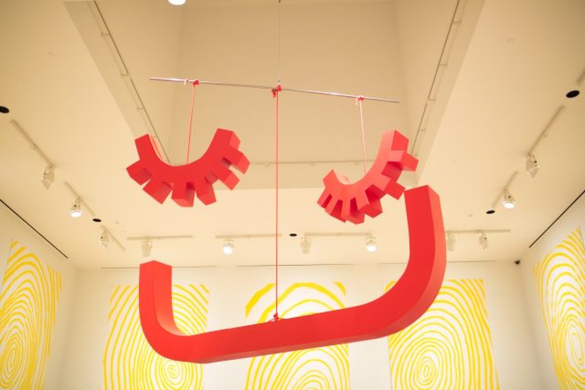 a red sculpture in three parts hangs from a ceiling