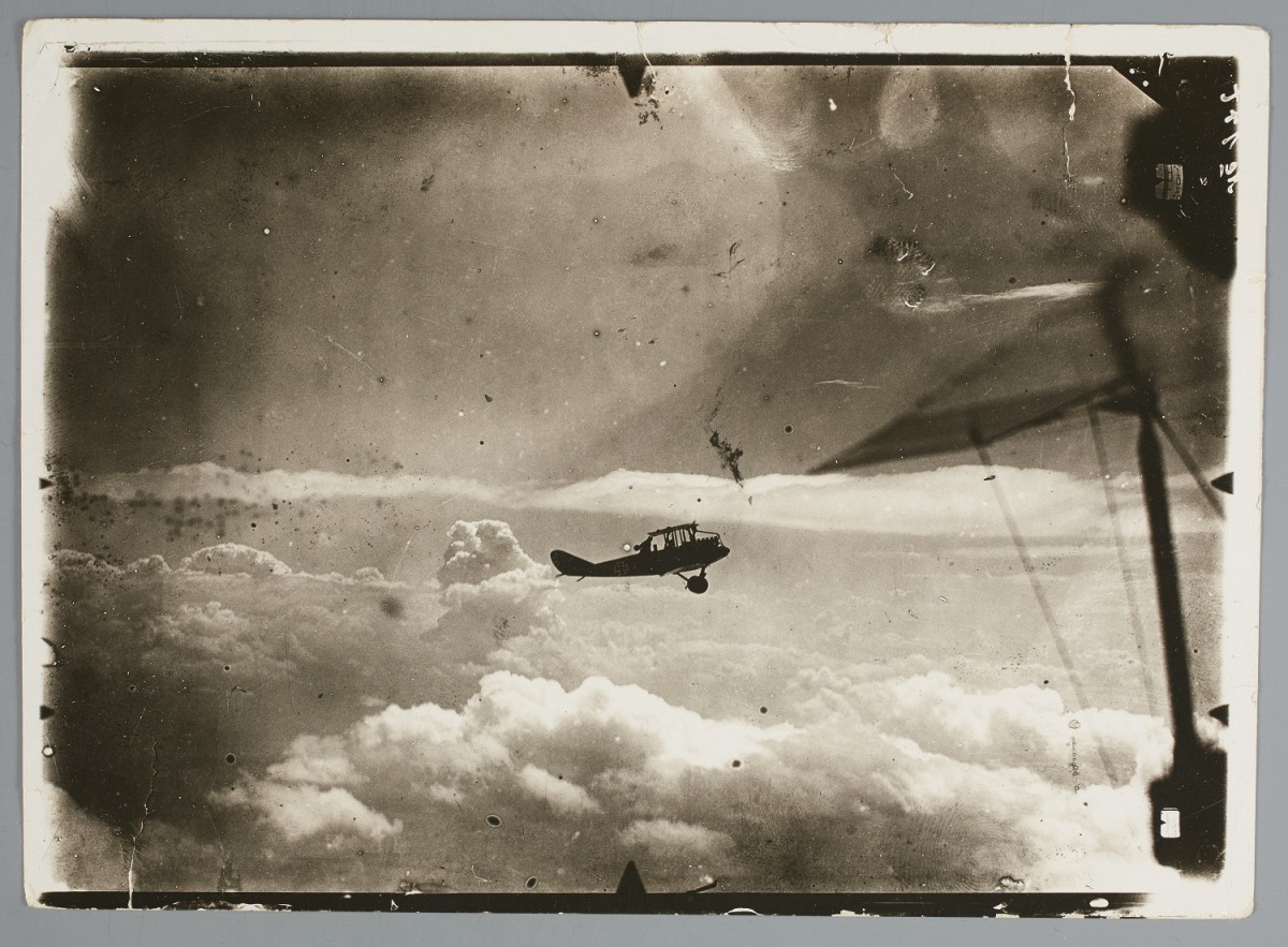 A photo from between 1914 and 1918 of a plane in flight, silhouetted against the sky.