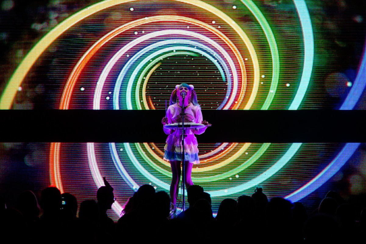 Clara Venice plays the theremin in front of an audience against a neon spiral backdrop.