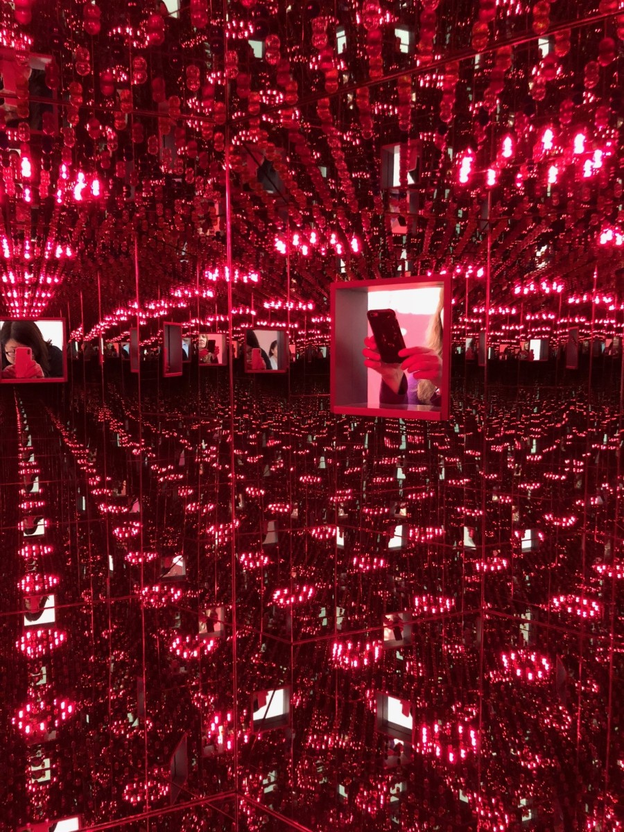 Two people taking pictures with their phones of a brightly lit Infinity Mirror Room.