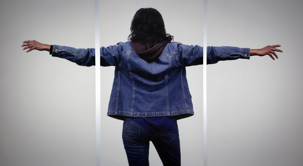 Three large photo panels depicting the back of a woman with brown hair, blue jean jacket and pants, arms outstretched to the side.