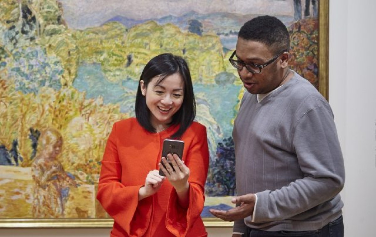 A man and a woman look at a phone in front of a painting