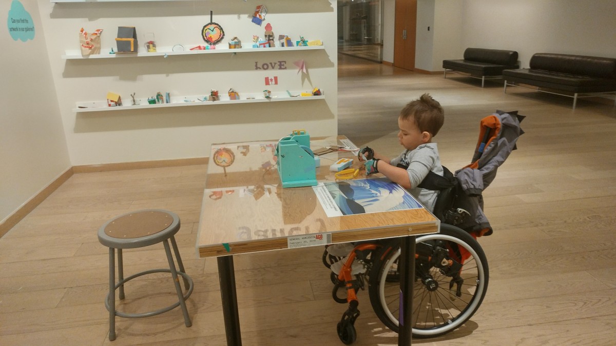 Noah is sitting in his wheelchair at the Mindful Makers exhibit at the AGO.