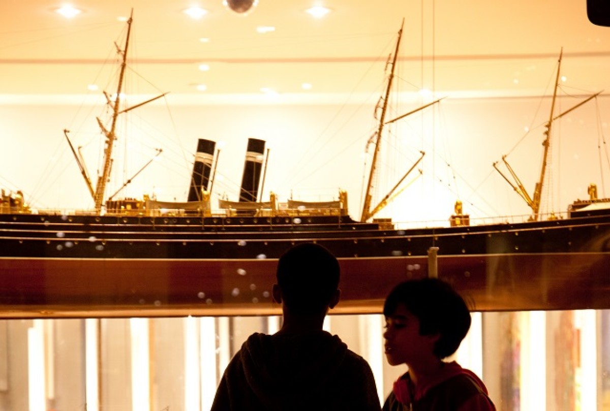 Two young boys look at a model ship encased in glass. 